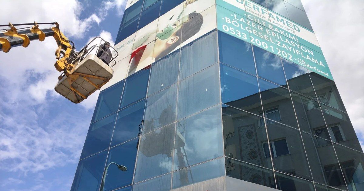 Sepetli vinçle yüksek bir binanın cam cephesini temizleyen görevli