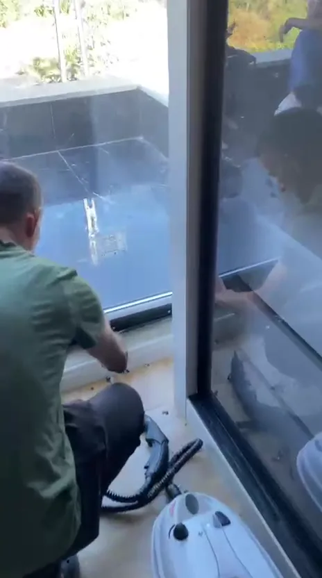 Ekip üyesi buharlı temizlik makinesiyle büyük cam kapının alt rayını temizliyor